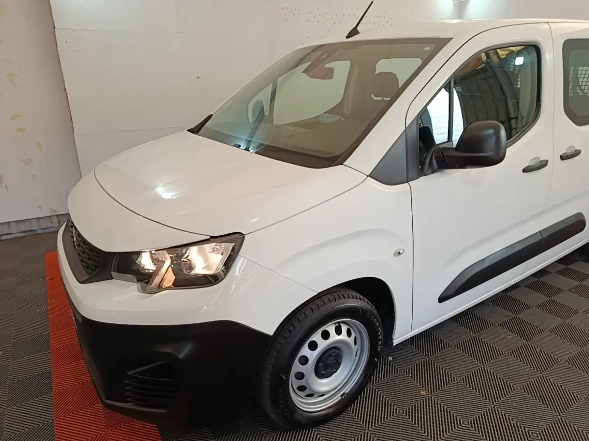 Vue 3/4 avant droit d’un Peugeot Partner blanc avec pare-chocs noirs et jantes acier simples.