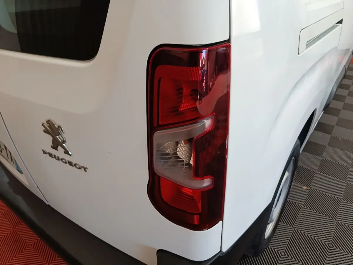 Gros plan sur le feu arrière droit d’un Peugeot Partner blanc, montrant le logo et la carrosserie arrière côté droit.