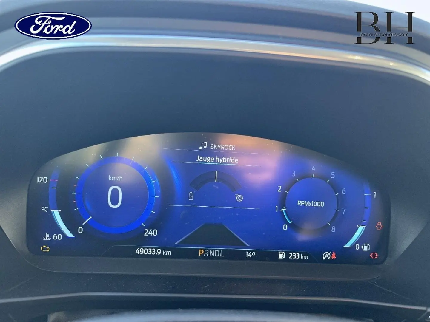 Tableau de bord numérique bleu de la Ford Focus 2023, affichant vitesse, régime et jauge hybride.