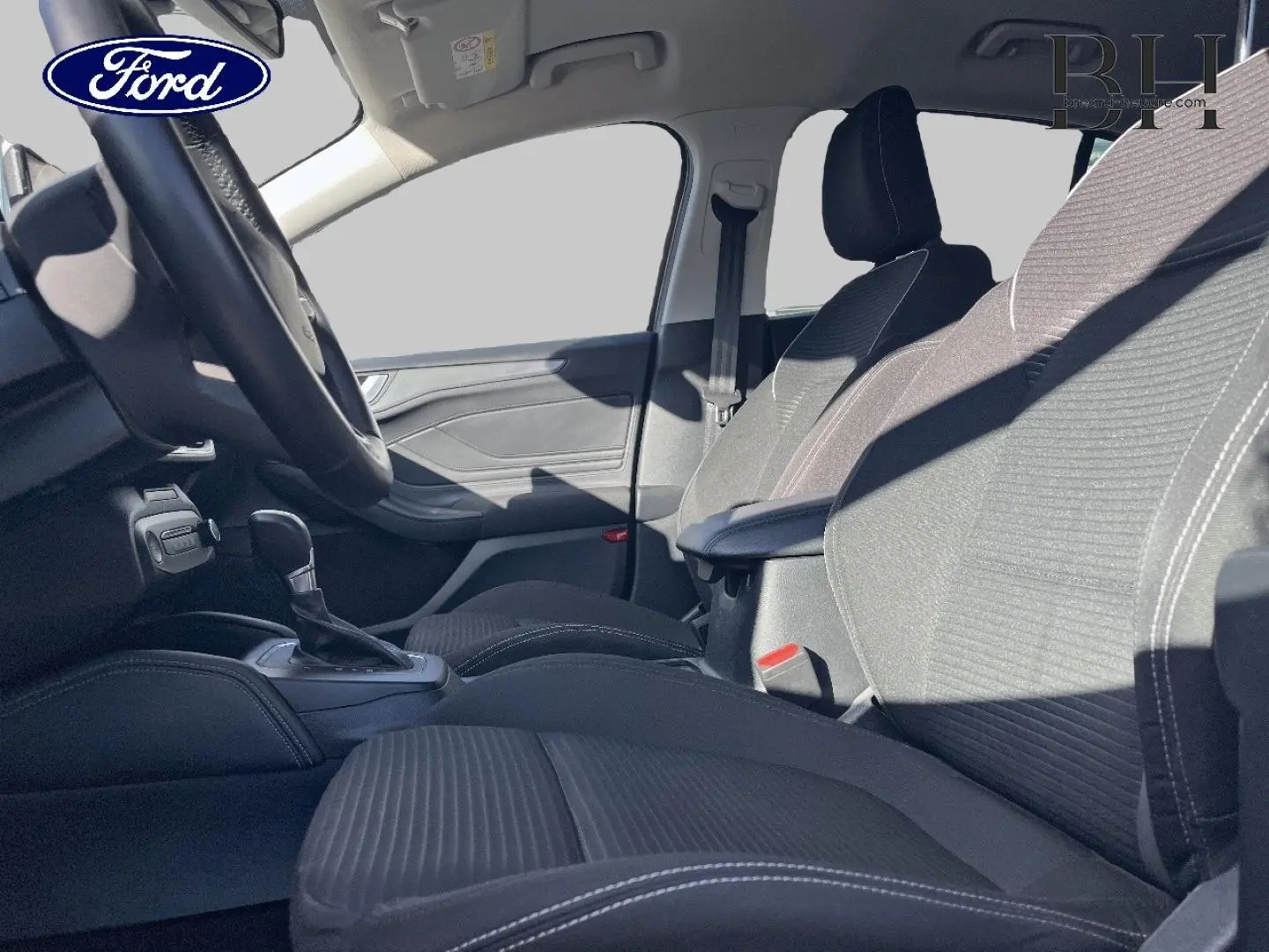 Vue intérieure côté conducteur de la Ford Focus 2023, sièges tissu noir avec surpiqûres blanches et accoudoir central.