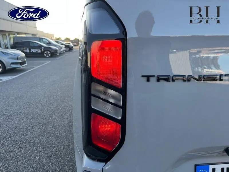 Gros plan sur le feu arrière gauche rouge et gris du Ford Transit Custom gris Matter, avec logo et partie arrière visible.