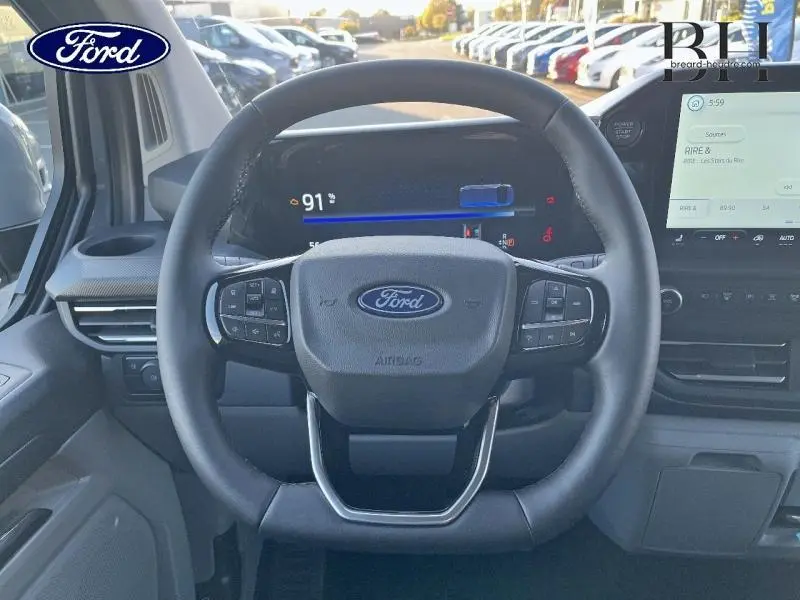 Vue frontale du volant Ford gris du Transit Custom Fourgon 2025 avec tableau de bord numérique et écran tactile central.