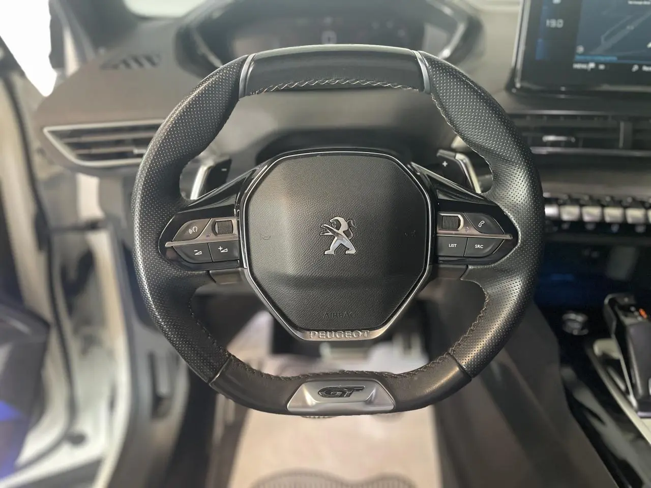 Vue rapprochée du volant cuir perforé noir avec logo GT du Peugeot 3008 blanc nacré, tableau de bord en arrière-plan.