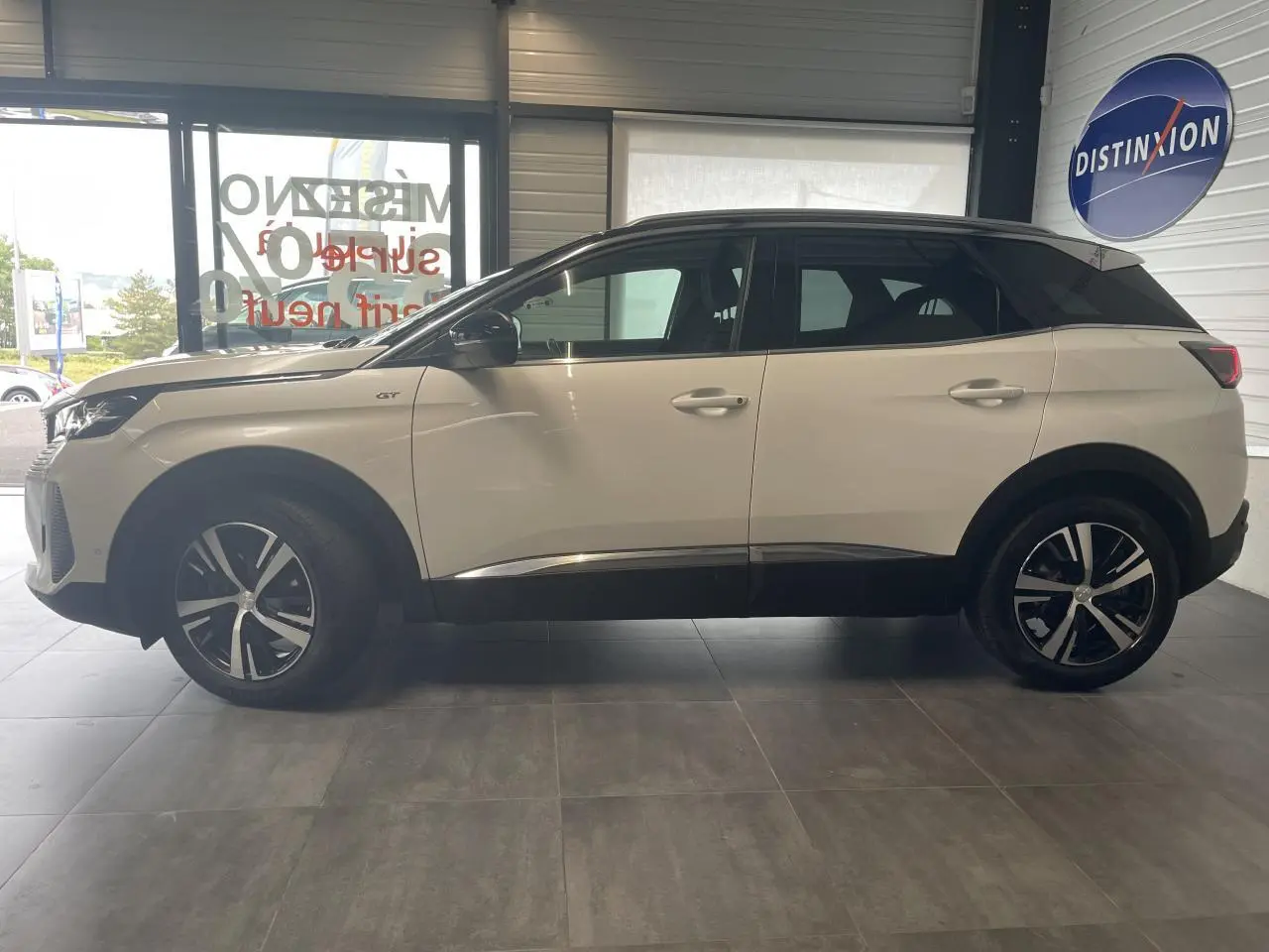 Peugeot 3008 GT blanc nacré vue de profil côté gauche, toit noir et jantes alliage bi-ton visibles en intérieur showroom.