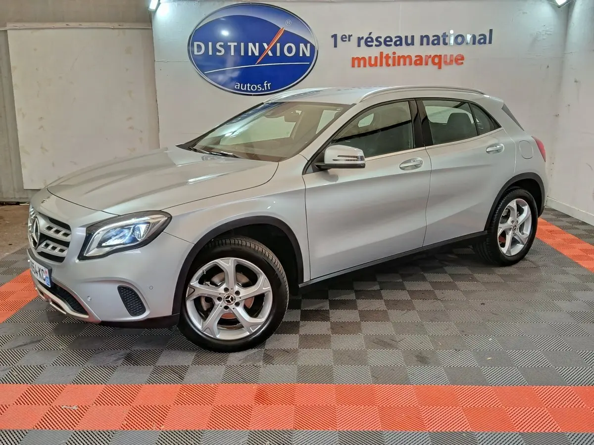 Mercedes GLA 200 d gris clair vue 3/4 avant droit en intérieur avec jantes alliage et phares LED allumés.