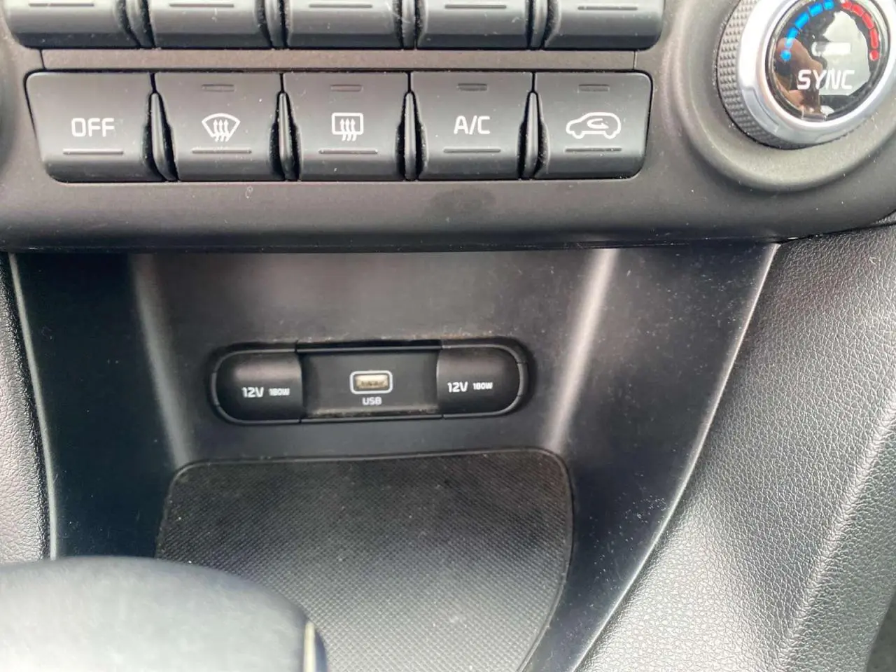 Détail de la console centrale avec commandes climatisation, prises 12V et port USB sur KIA Sportage gris foncé.