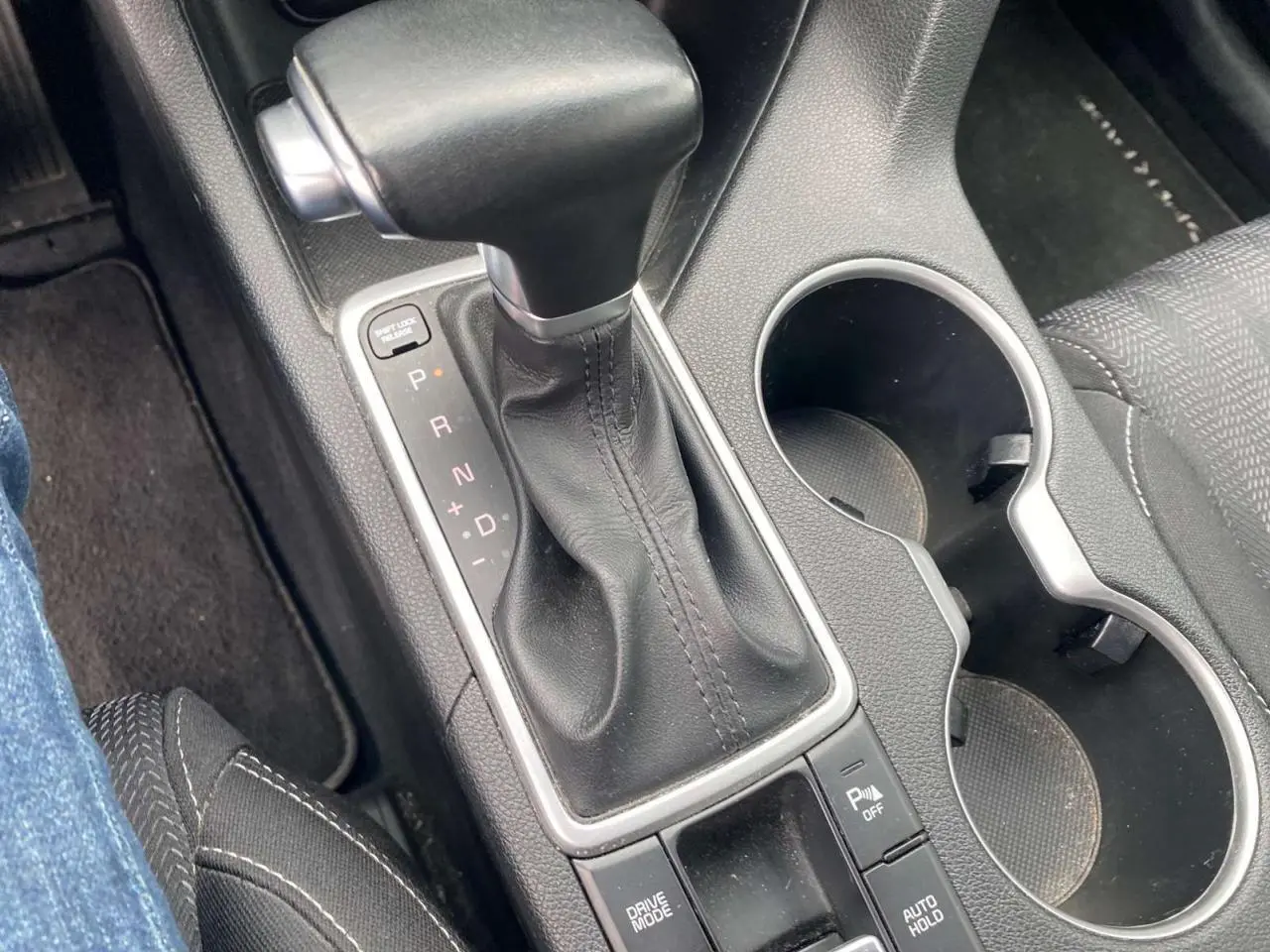 Gros plan sur la console centrale du Kia Sportage 2021, levier de vitesses cuir noir et porte-gobelets.