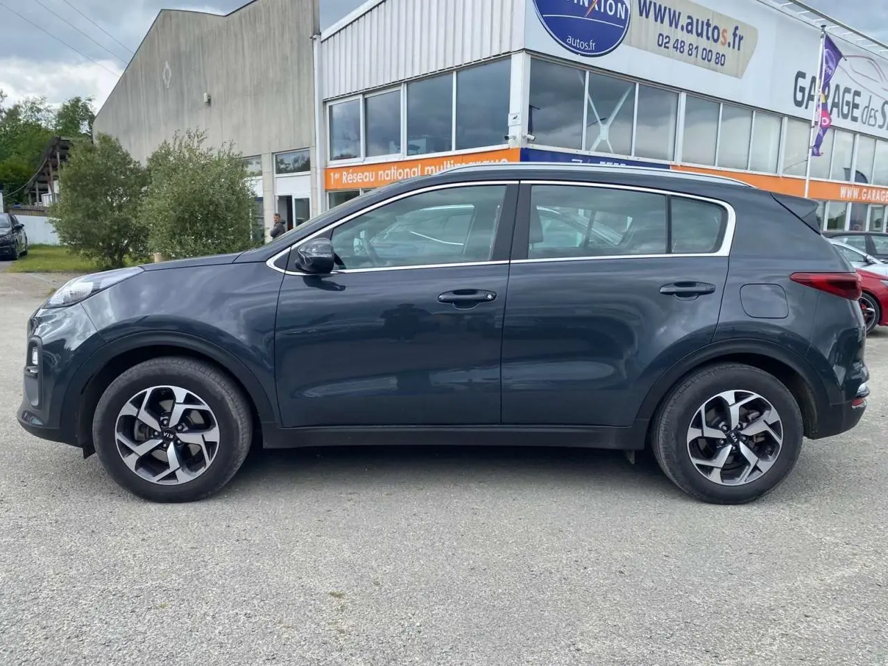 Vue de profil côté gauche d'un KIA Sportage gris foncé 2021 avec jantes alliage noires Black Edition.