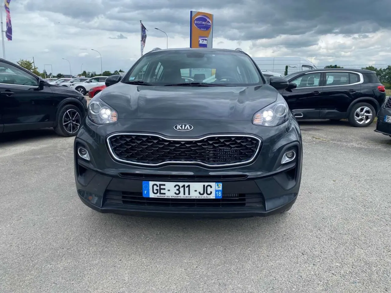 Vue de face du KIA Sportage gris foncé avec calandre noire et phares allumés sur un parking extérieur.