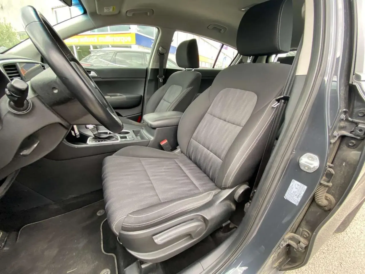 Vue intérieure côté conducteur du Kia Sportage gris foncé 2021, mettant en valeur le siège avant et le volant cuir.