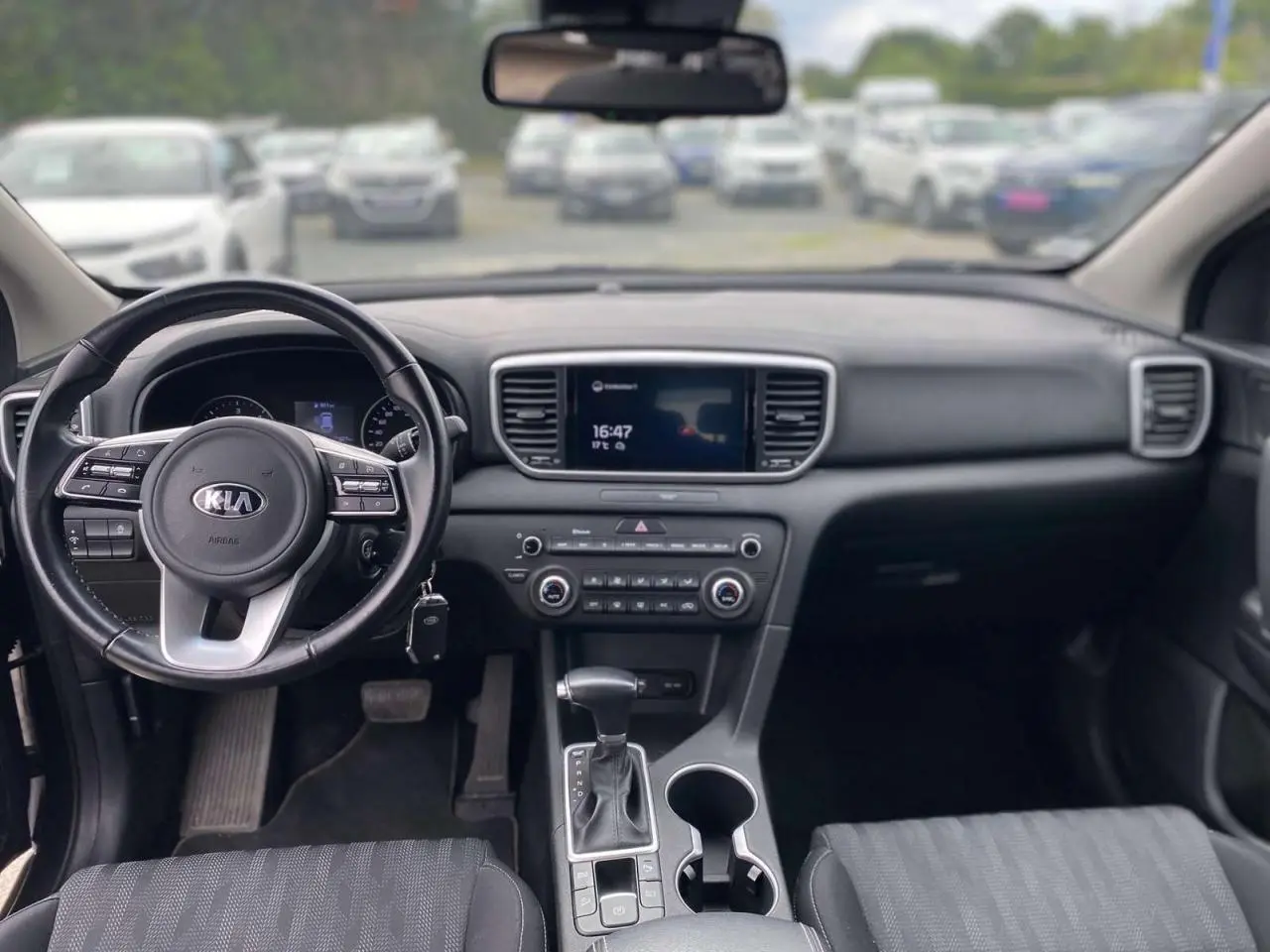 Vue intérieure avant du Kia Sportage 2021, tableau de bord noir avec volant cuir et écran tactile central.
