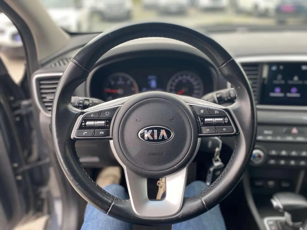 Vue centrée sur le volant cuir noir du Kia Sportage 2021, avec tableau de bord et écran tactile en arrière-plan flou.