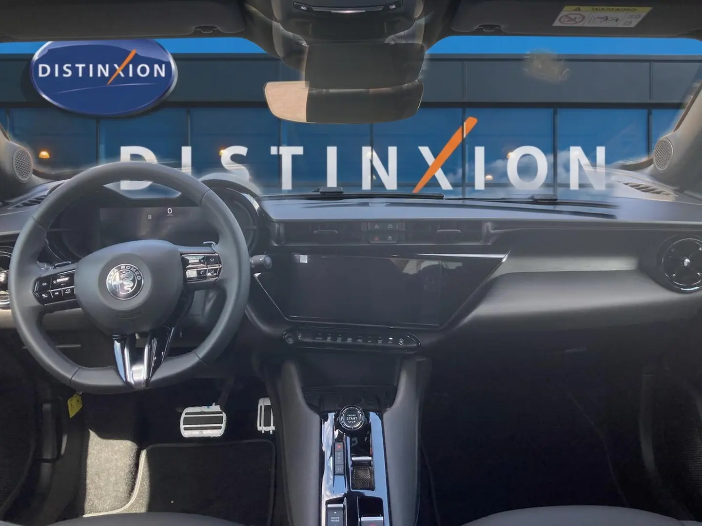Vue intérieure frontale de l'Alfa Romeo Junior 1.2 hybride 2026, tableau de bord noir avec écran tactile et volant multifonction.