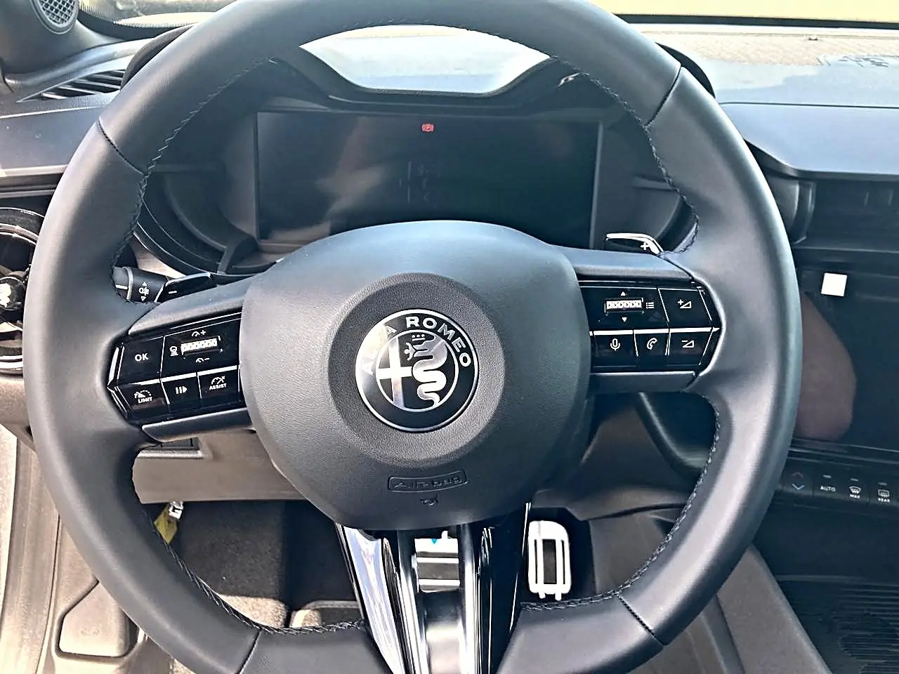 Vue rapprochée du volant noir de l'Alfa Romeo Junior 1.2 hybride, avec commandes intégrées et tableau de bord numérique.