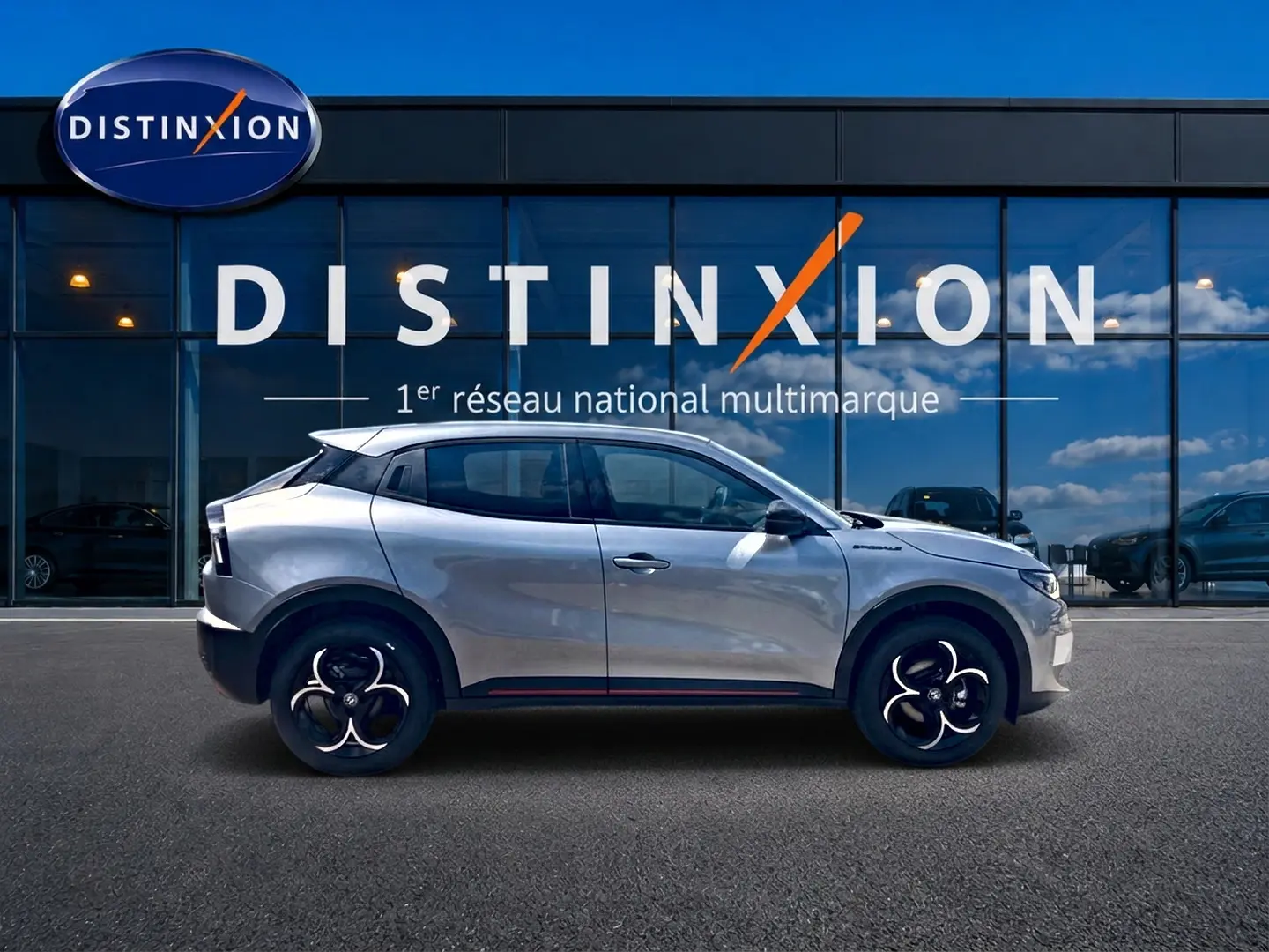 Vue de profil côté gauche d'une Alfa Romeo Junior grise garée devant une vitrine avec logo Distinxion.
