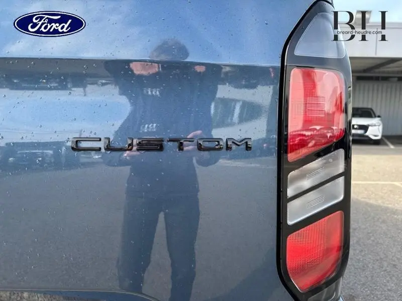 Gros plan sur le feu arrière droit et l'inscription Custom du Ford Transit Custom bleu azur métallisé 2025.