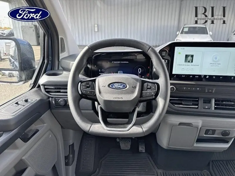 Vue frontale du poste de conduite du Ford Transit Custom hybride rechargeable 2025 avec volant multifonction et écran tactile large.