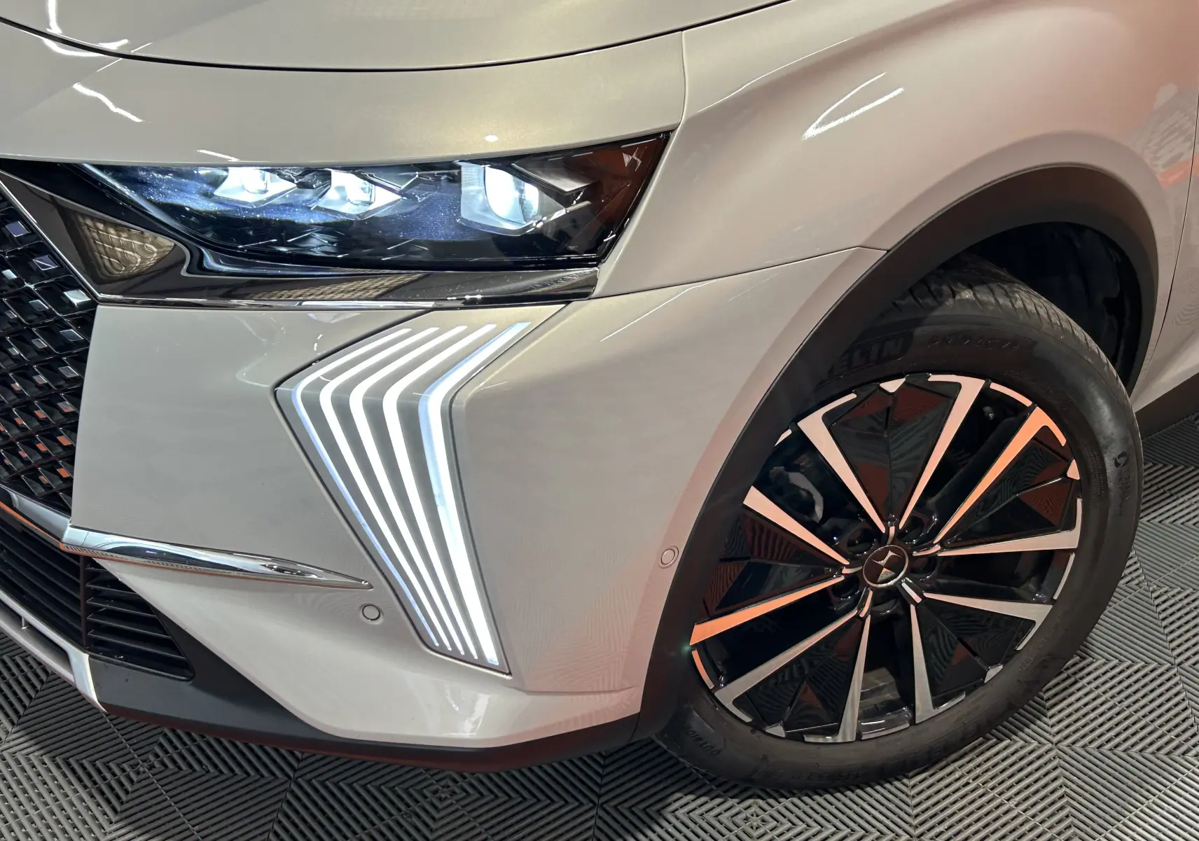 Gros plan sur l'avant droit du DS7 2024 Chrystal pearl, mettant en valeur le phare LED et la jante noire et chrome.