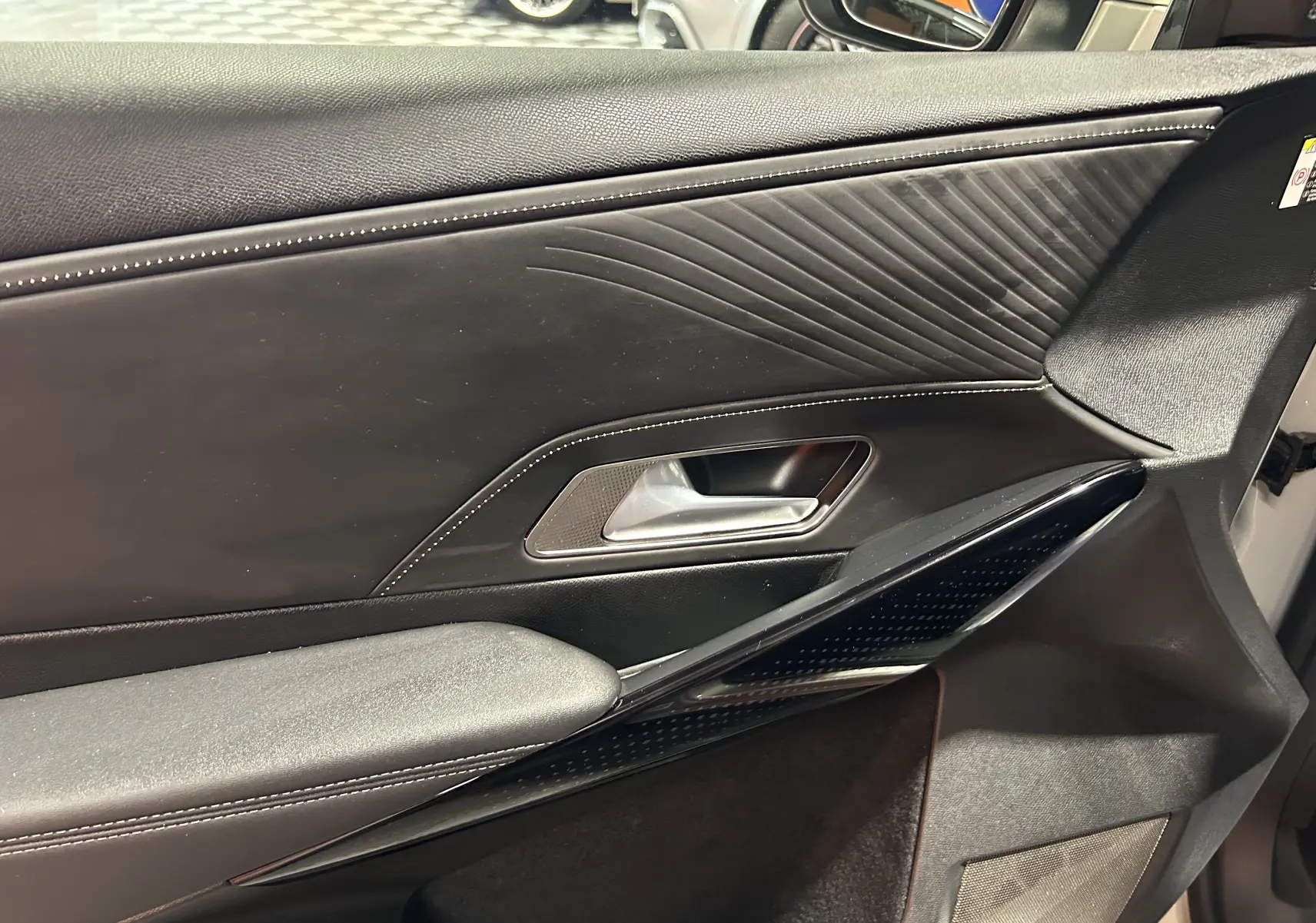 Gros plan sur la garniture intérieure noire de la porte côté gauche du DS7 2024 avec surpiqûres blanches et poignée argentée.