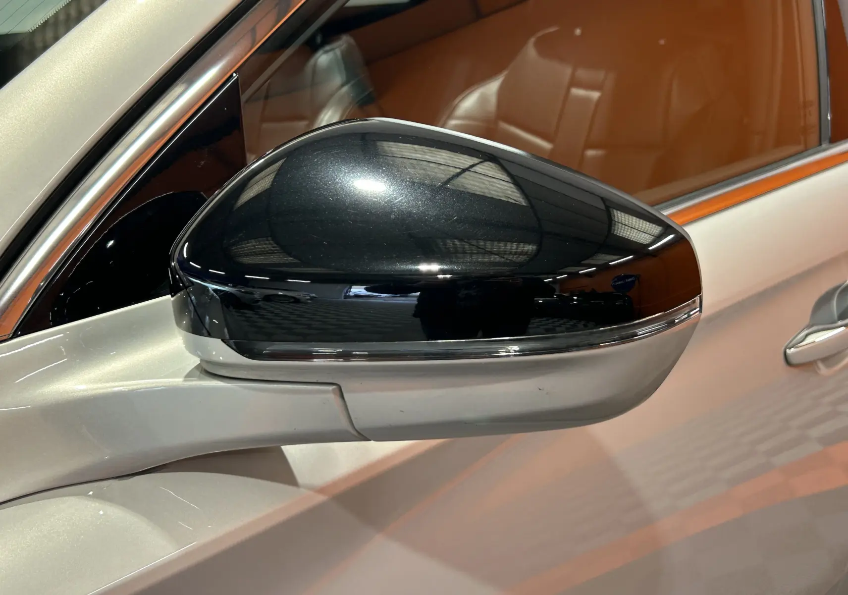 Rétroviseur noir brillant côté gauche sur DS7 Chrystal pearl 2024 avec intérieur cuir marron visible au travers.