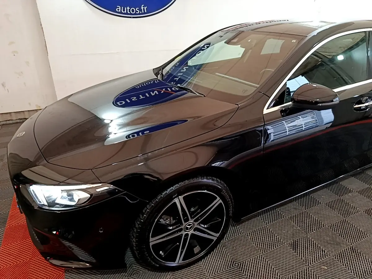 Vue 3/4 avant droite d'une Mercedes Classe A berline noire avec jantes alliage et phares LED allumés.