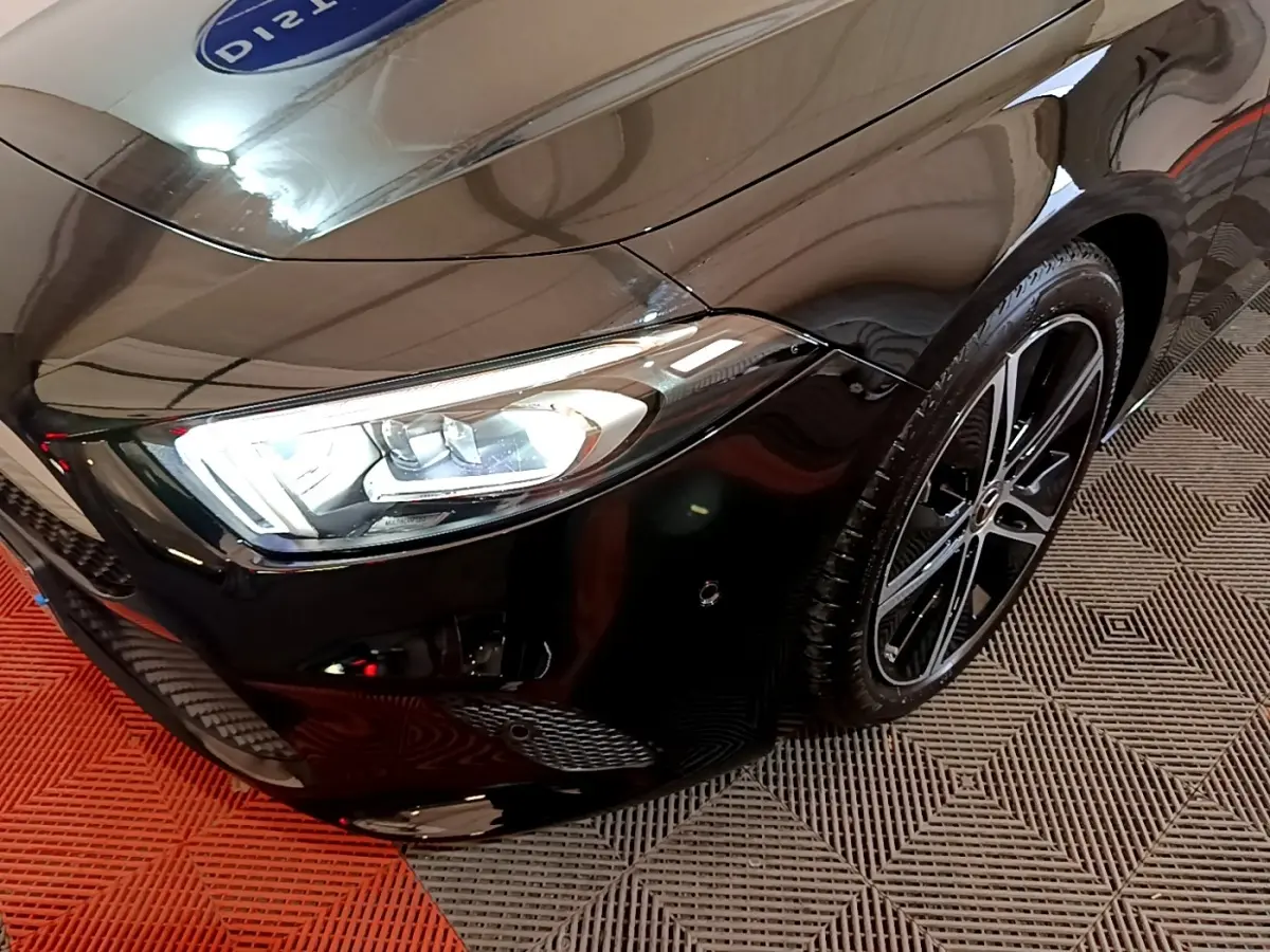 Gros plan sur l'avant droit noir brillant d'une Mercedes Classe A Berline 2022 avec phares LED et jante alliage.