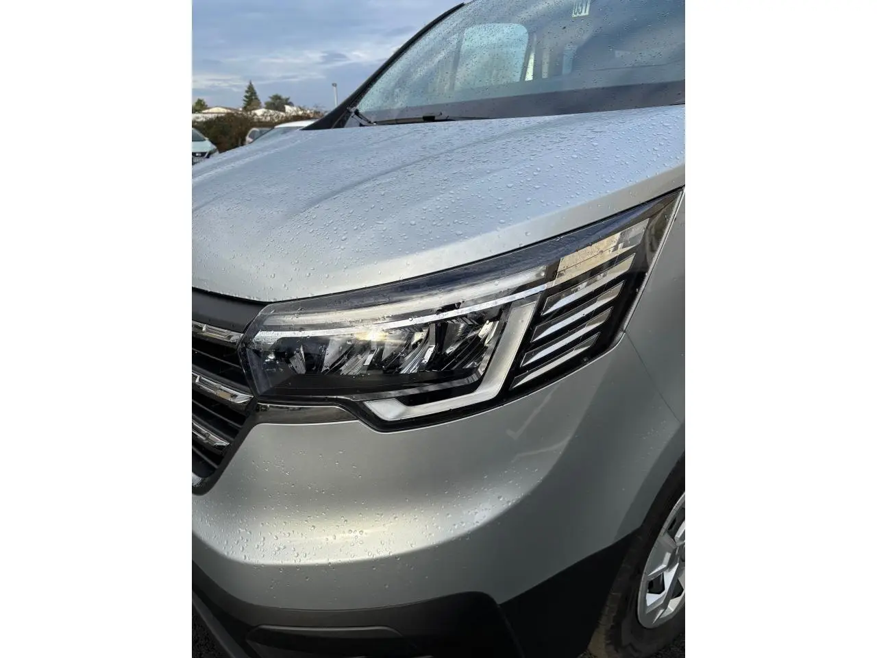 Gros plan sur l'avant droit gris clair du Renault Trafic Fourgon 2022, mettant en valeur le phare LED et la calandre humide.