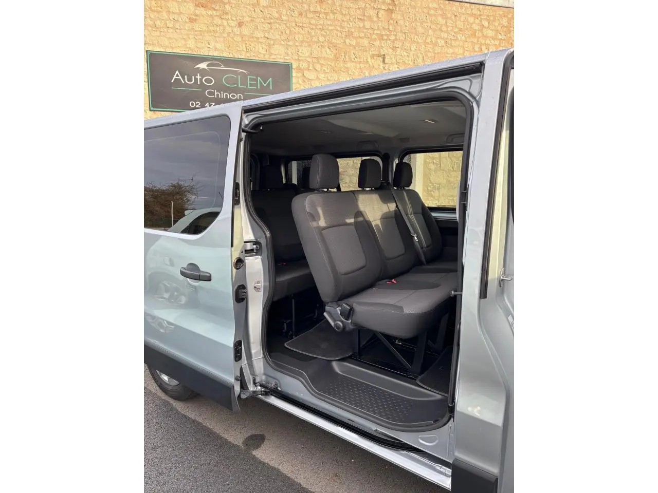 Vue latérale gauche du Renault Trafic Fourgon gris clair 2022 avec porte coulissante ouverte montrant les sièges passagers en tissu noir.