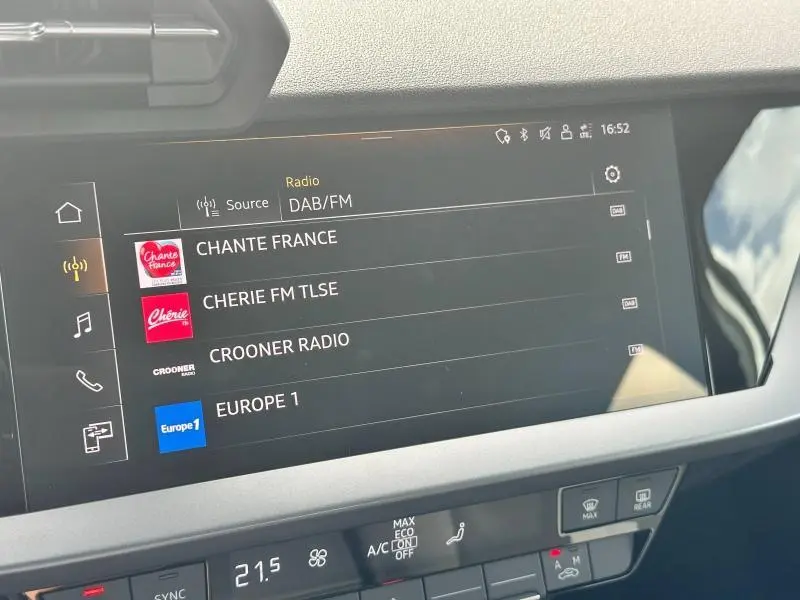Écran tactile central de l'Audi A3 Sportback 2024 affichant les stations radio DAB/FM, avec commandes climatisation en dessous.
