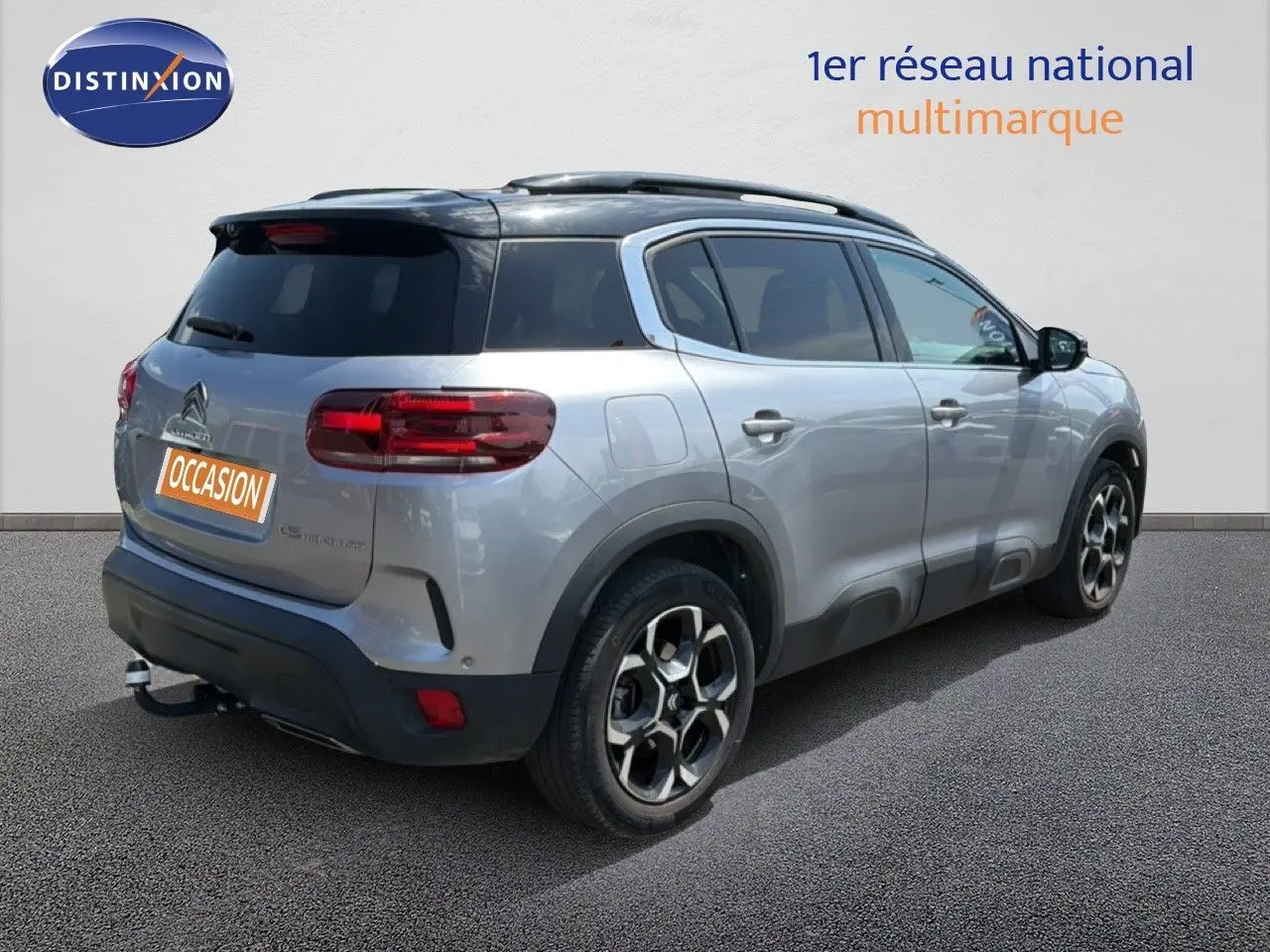 Vue 3/4 arrière droite d'un Citroën C5 Aircross gris acier avec toit noir et jantes bi-ton, stationné sur sol gris.