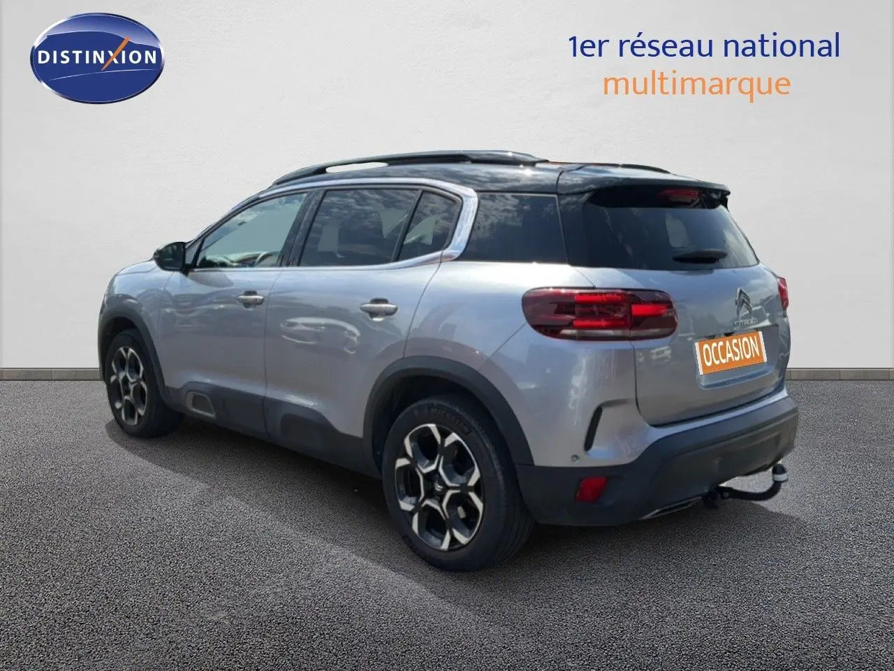 Vue 3/4 arrière droite d'un Citroën C5 Aircross gris acier avec toit noir et jantes bi-ton, stationné devant un mur blanc.