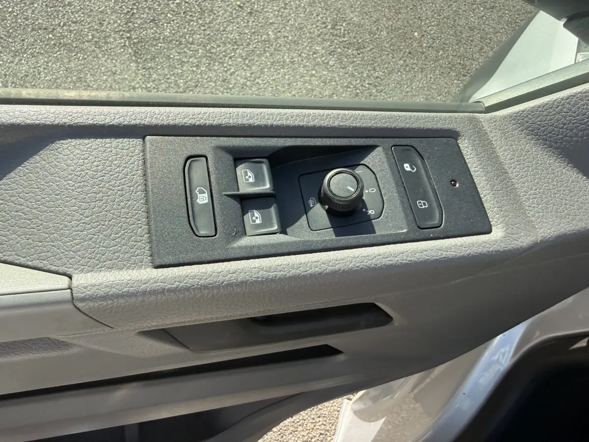 Détail des commandes de réglage des rétroviseurs et des vitres sur la porte côté conducteur d’un Volkswagen Transporter gris clair.