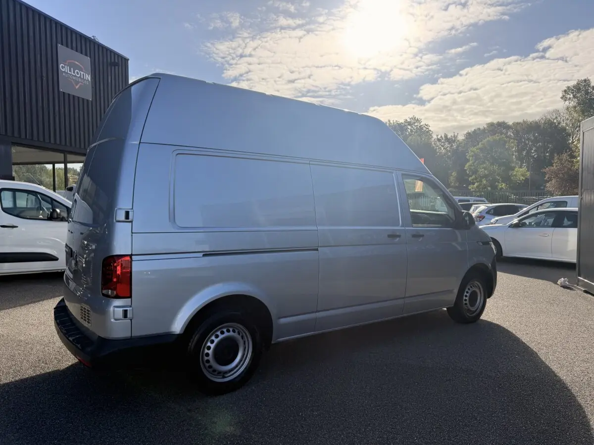 Vue 3/4 arrière droit d’un Volkswagen Transporter gris clair L2H1 avec grande hauteur de toit, stationné en extérieur.
