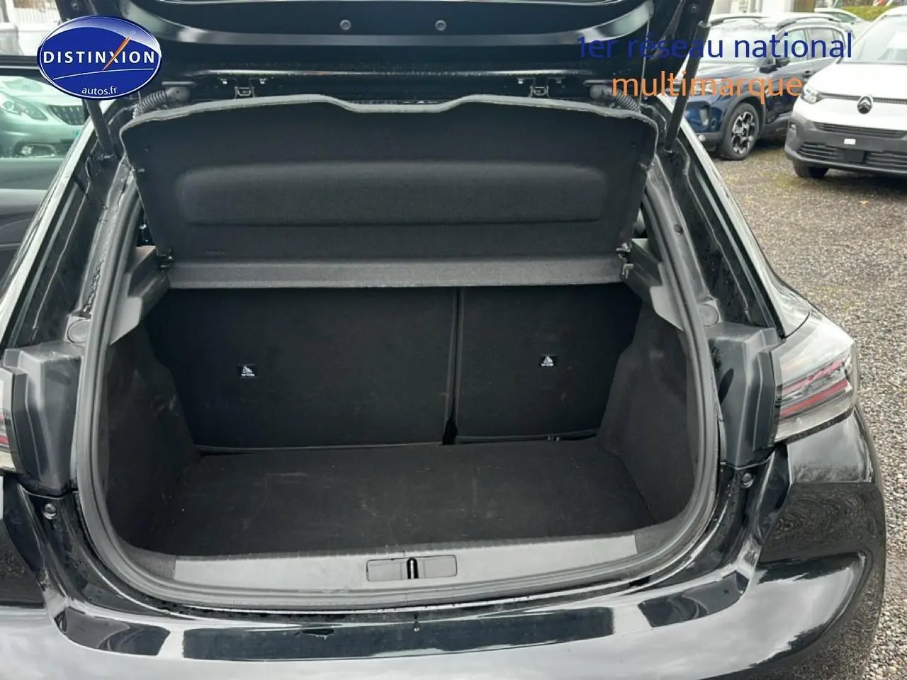 Coffre ouvert vu de l'arrière d'une Peugeot 208 noire, montrant un espace de chargement vide et propre.
