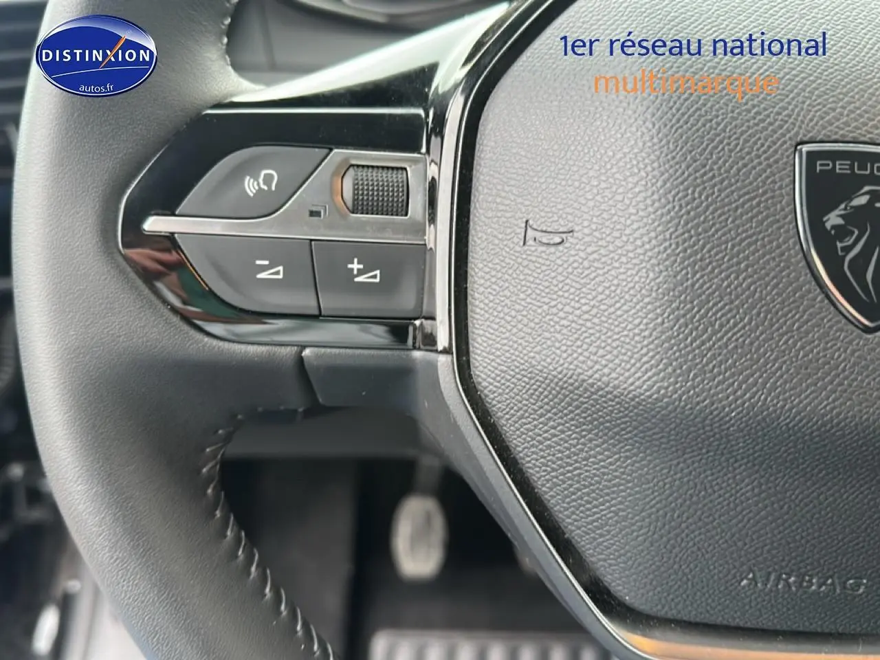 Gros plan sur le volant noir de la Peugeot 208 1.2 100 style avec commandes audio intégrées à gauche.