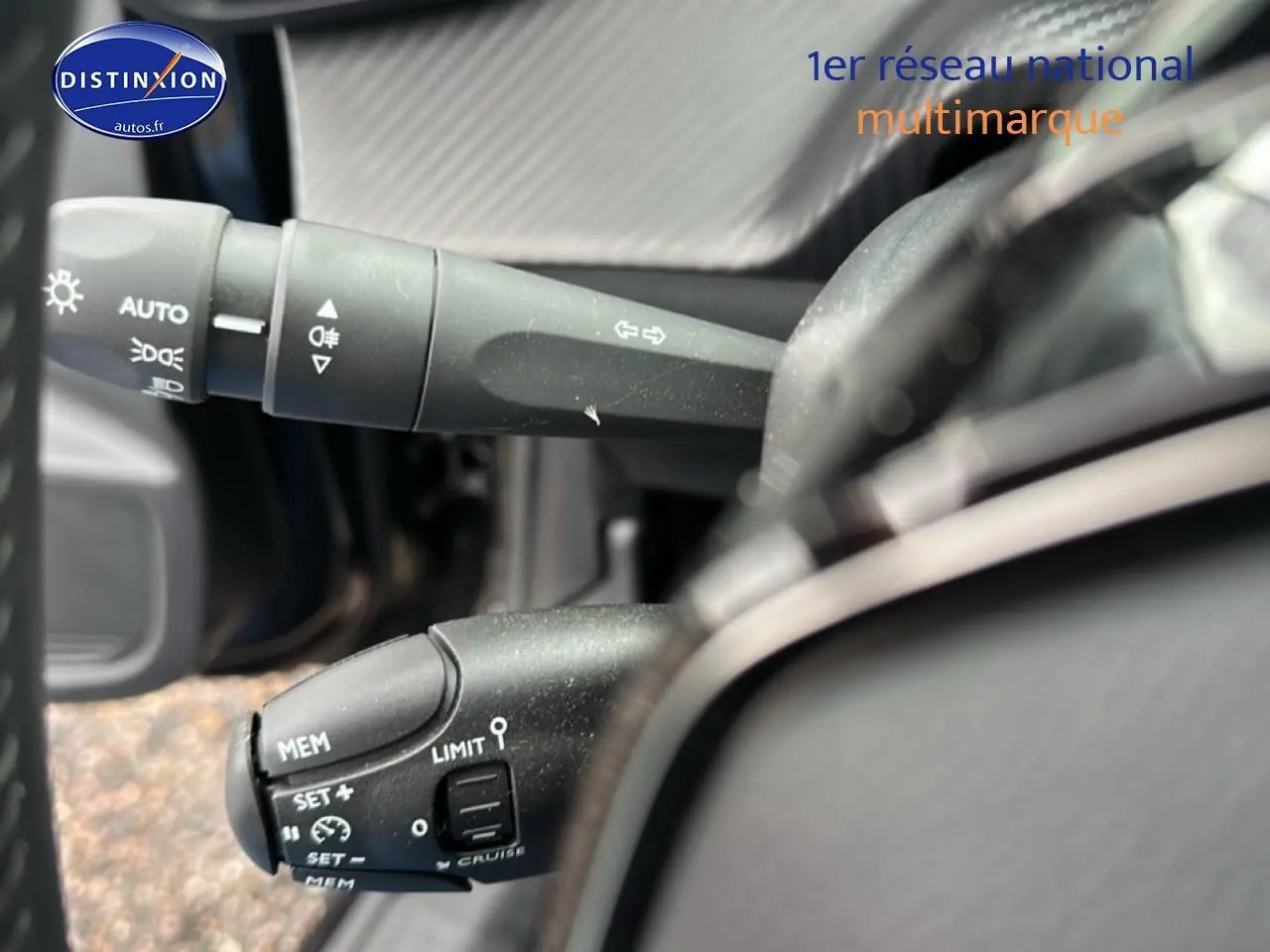 Gros plan sur les commandes au volant de la Peugeot 208 noire, mettant en valeur les fonctions de régulateur et feux.