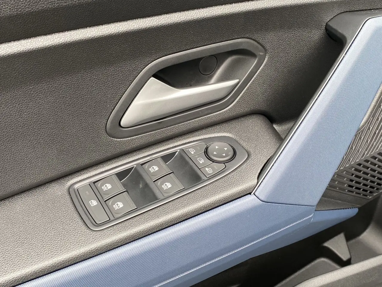 Détail de la porte avant gauche du Dacia Duster 2025 avec commandes de vitres et poignée argentée, garniture bleu et noire.