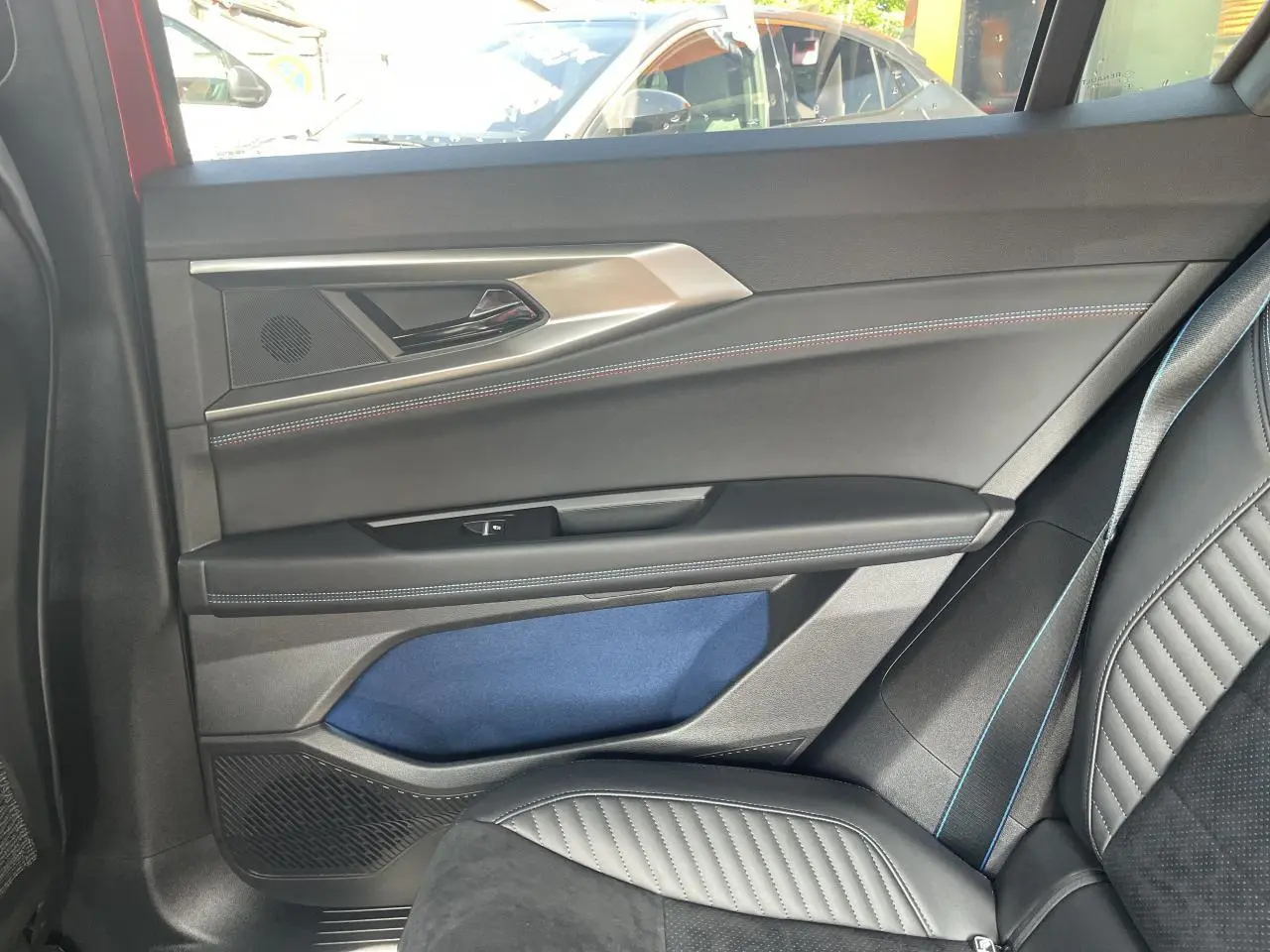 Intérieur côté droit arrière de Renault Rafale rouge, avec porte noire, surpiqûres bleues et siège en cuir noir.