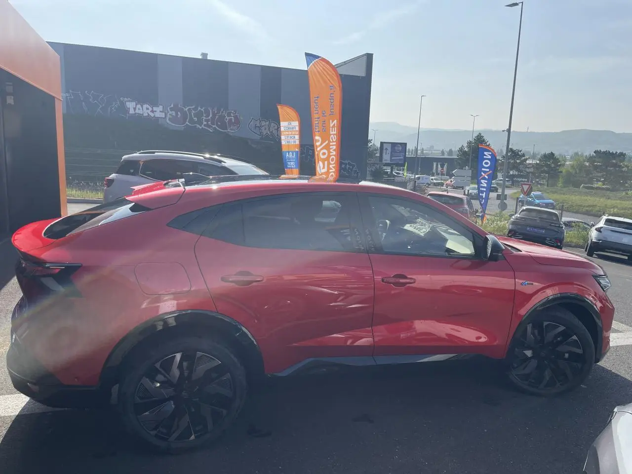 Profil côté gauche d'un Renault Rafale rouge flamme avec toit noir, jantes noires et badge Esprit Alpine visible.