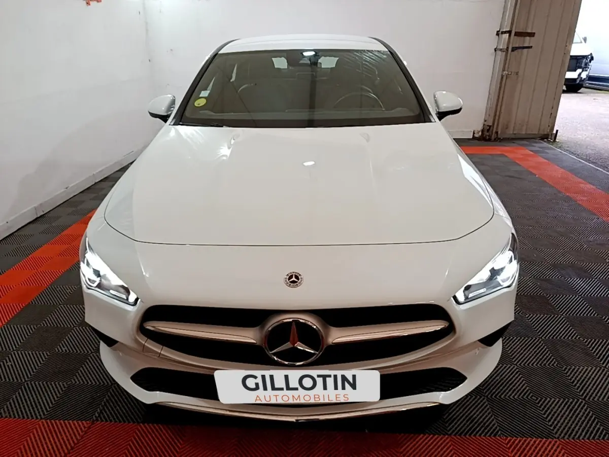 Vue avant d'une Mercedes CLA 200 d Business Line blanche avec phares LED allumés dans un garage.