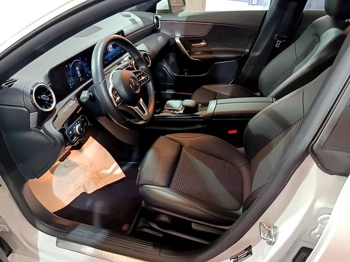 Vue intérieure côté conducteur de la Mercedes CLA 200 d Business Line blanche, avec tableau de bord digital et sièges noirs.