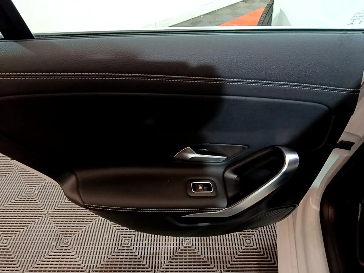 Vue intérieure du panneau de porte avant gauche noir avec poignée alu et bouton de verrouillage, Mercedes CLA 200 d blanc.