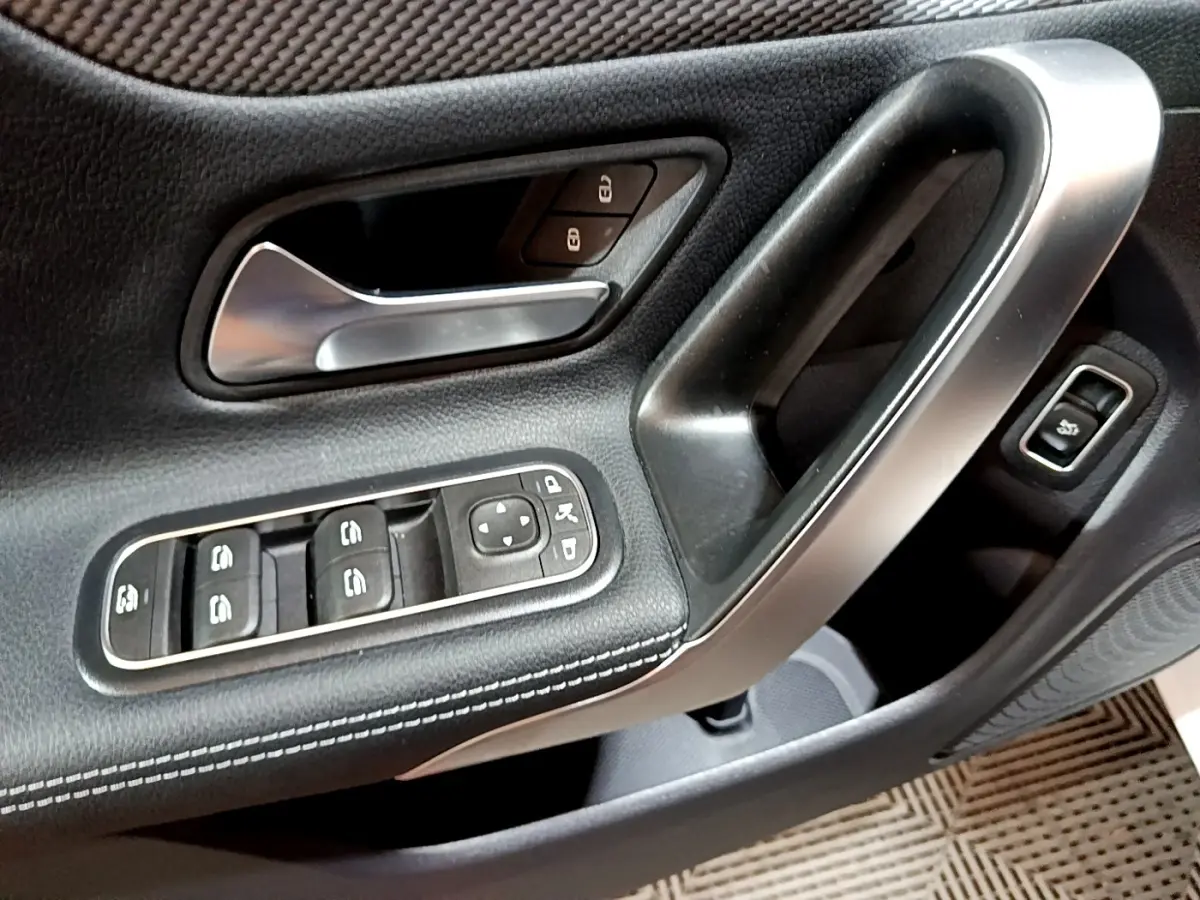 Gros plan sur la porte côté conducteur de la Mercedes CLA 200 d Business Line blanche, avec commandes électriques et poignée alu.