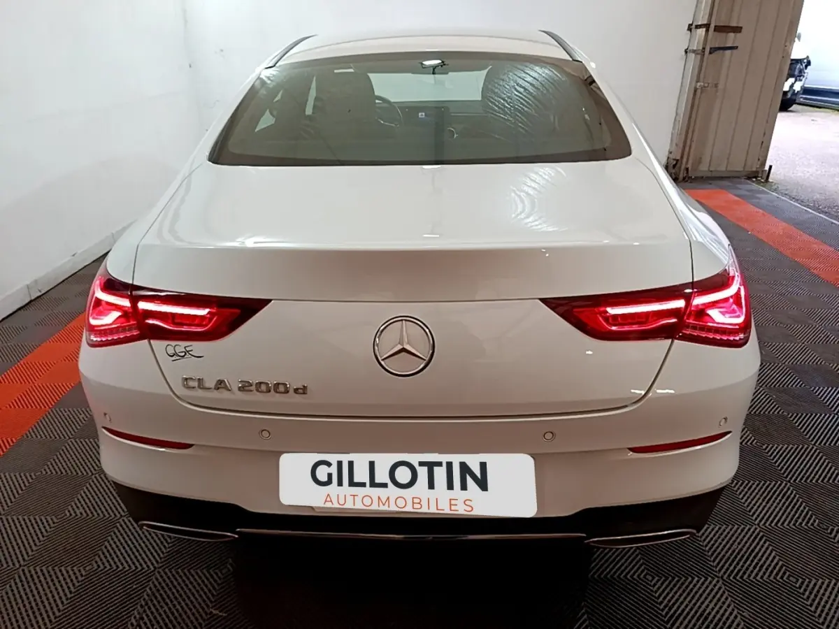 Vue arrière d'une Mercedes CLA 200 d Business Line blanche avec feux arrière LED allumés dans un garage.