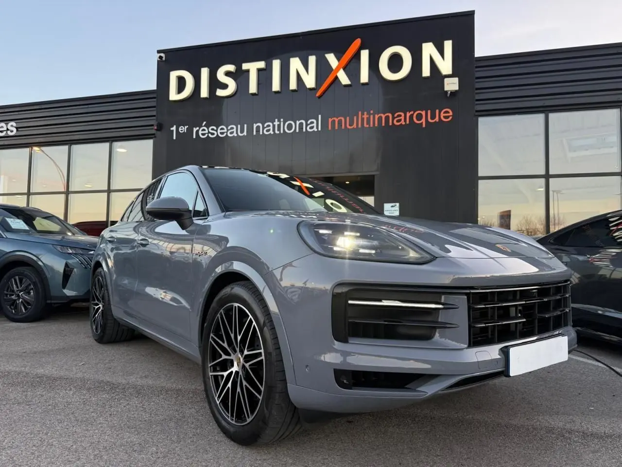 Vue 3/4 avant droite d’un Porsche Cayenne III Coupe 3.0 V6 S E-Hybrid 2024 en gris arctique avec jantes noires distinctives.