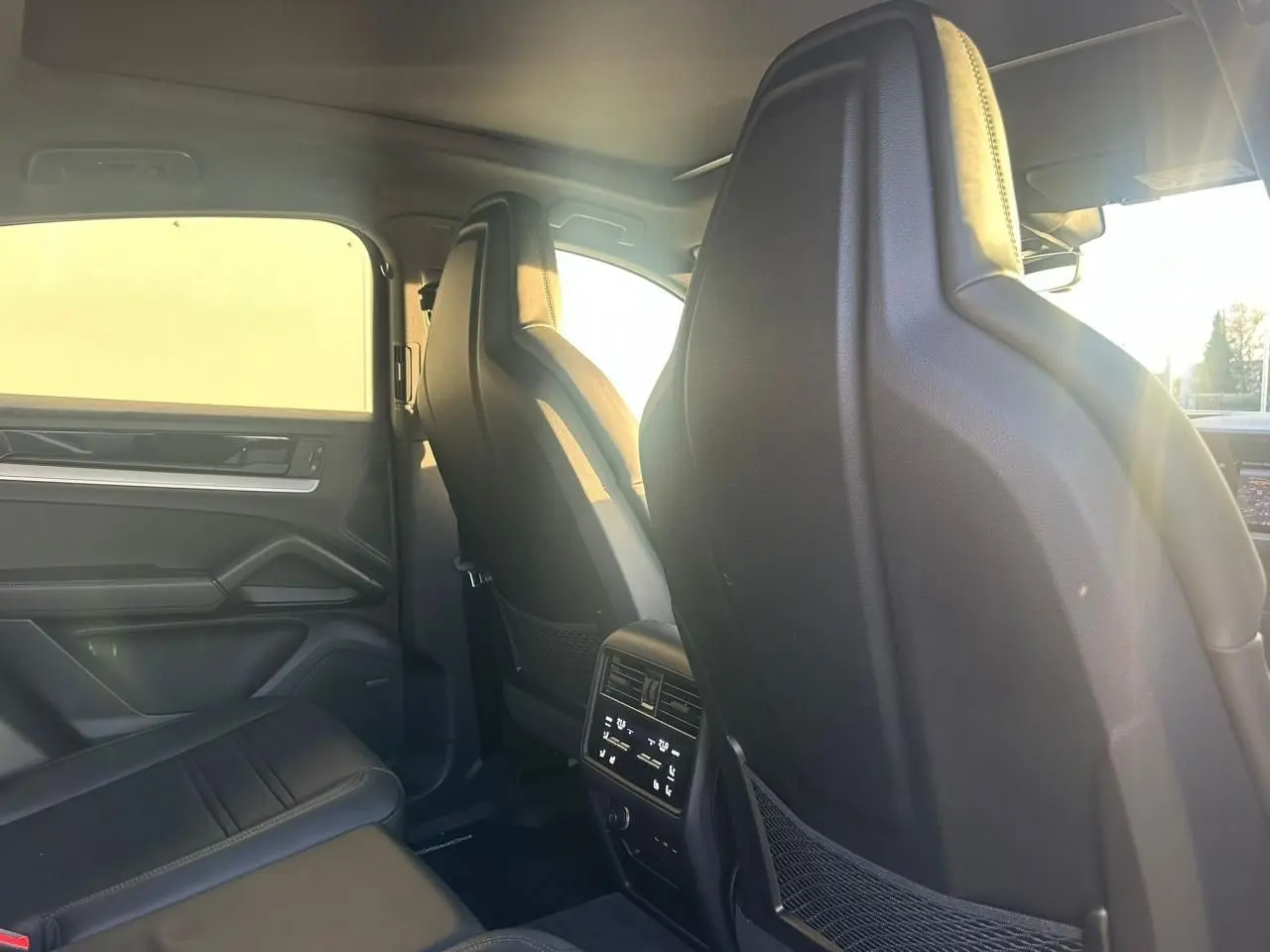 Vue intérieure arrière du Porsche Cayenne III Coupe 3.0 V6 S E-Hybrid 2024, montrant les sièges noirs et la console centrale arrière.