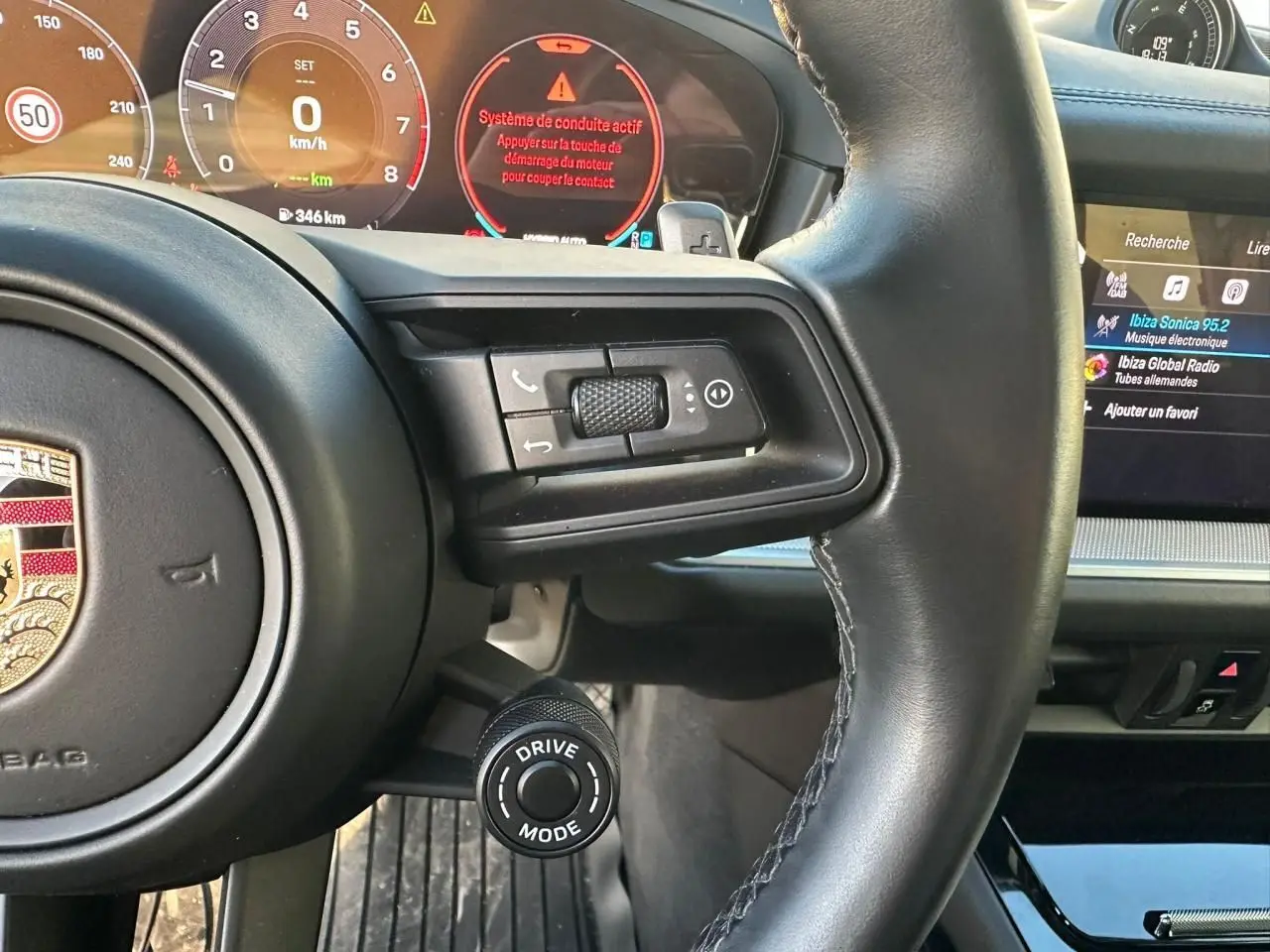 Vue rapprochée du volant noir du Porsche Cayenne 2024 avec commandes intégrées et affichage digital du tableau de bord.