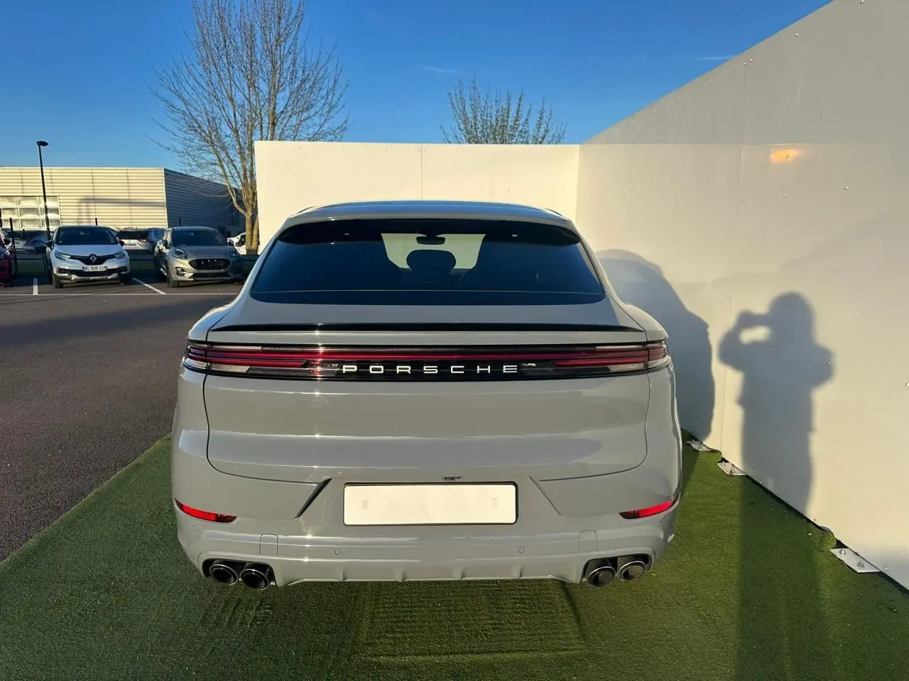 Vue arrière d'un Porsche Cayenne III Coupe 3.0 V6 S E-Hybrid 2024 en gris arctique avec feux LED continus et double sortie d'échappement.