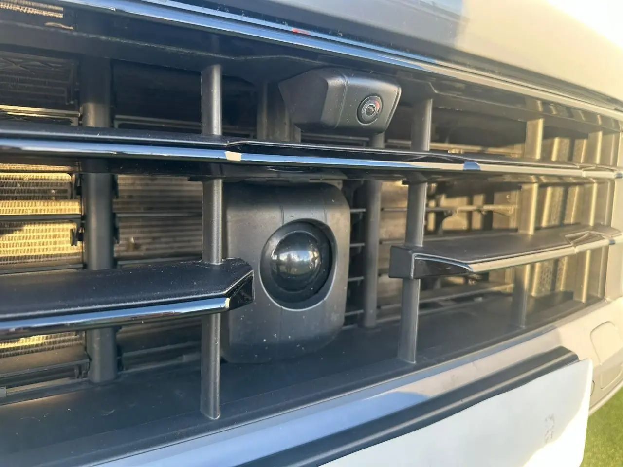 Gros plan sur la calandre avant noire du Porsche Cayenne 2024 gris arctique, mettant en valeur la caméra et capteurs intégrés.