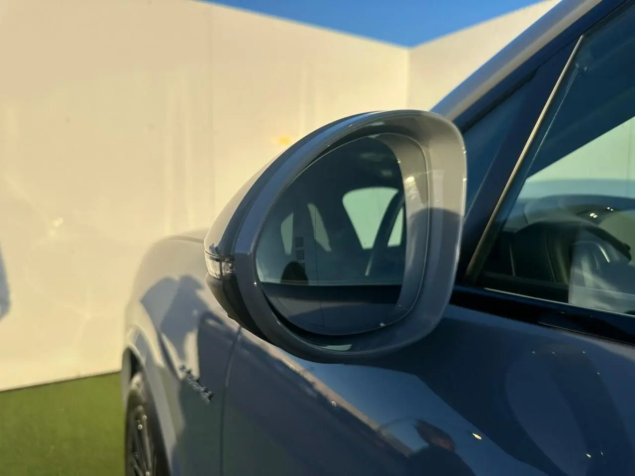 Gros plan sur le rétroviseur côté gauche d’un Porsche Cayenne Coupe 2024 gris arctique, avec reflet de l’habitacle visible.